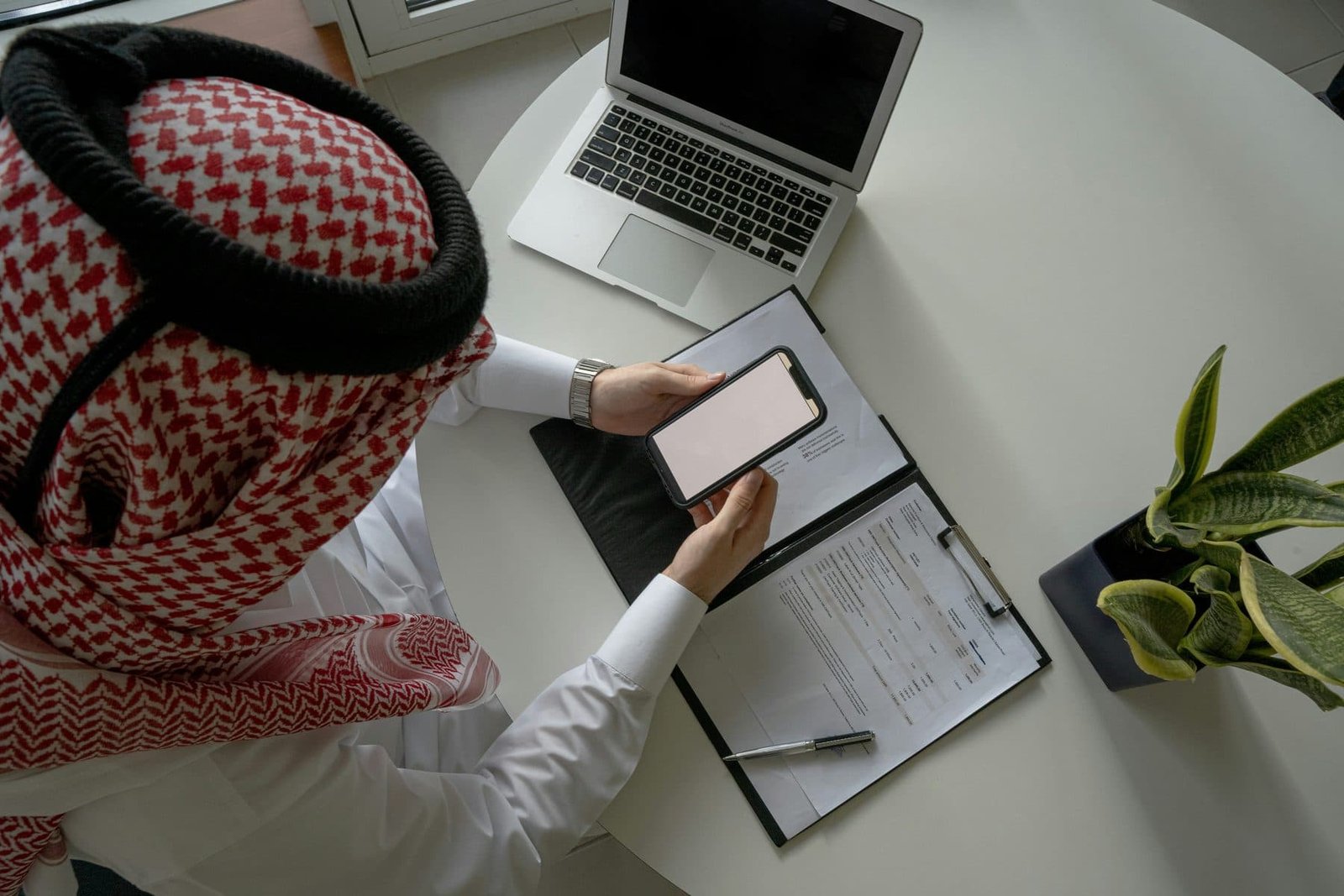 رجل أعمال سعودي يراجع المستندات المالية على الجوال واللابتوب